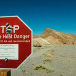 A red warning sign highlights extreme heat danger in a desert area.