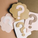 Question mark cutouts in layered paper craft style on a brown backdrop, conceptual art.