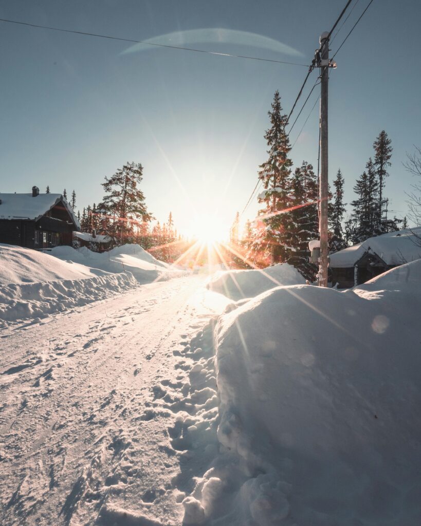 Serene winter sunrise illuminating a snowy path and trees in Sweden with dramatic sunrays.